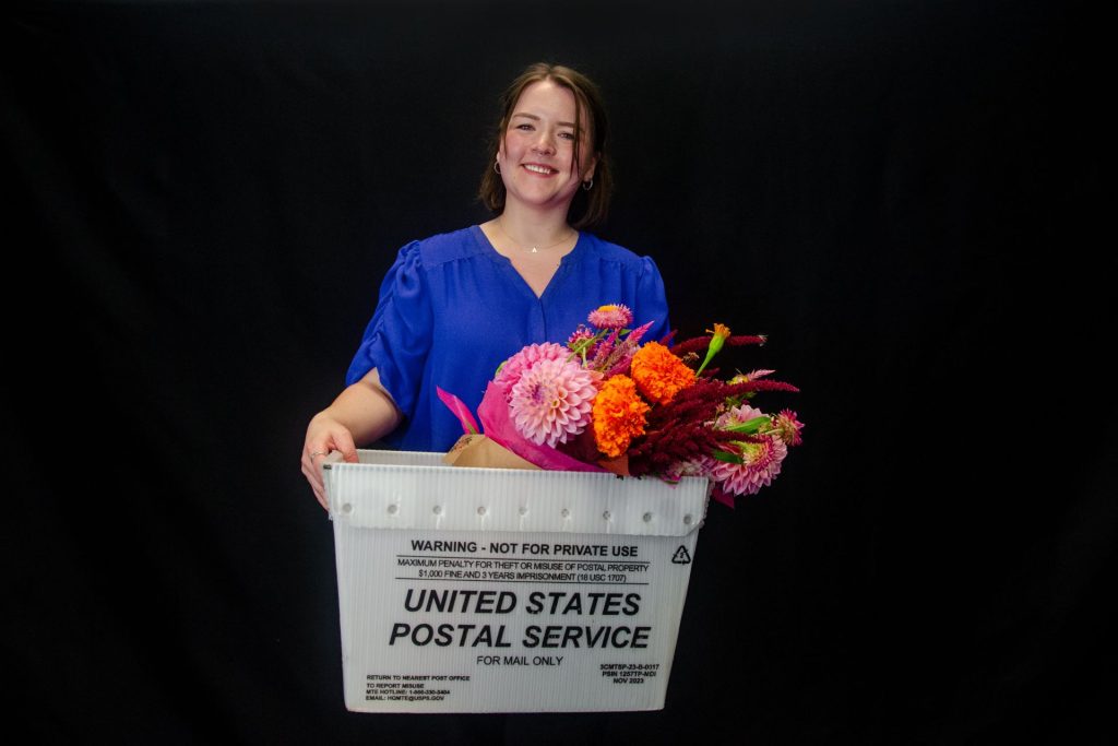 Abby, Mailstar Director of Operations, holding a USPS mail tub filled with flowers