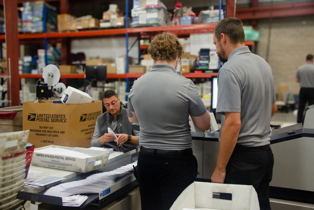 Mailstar production team checking mail pieces at an inserter beside USPS trays