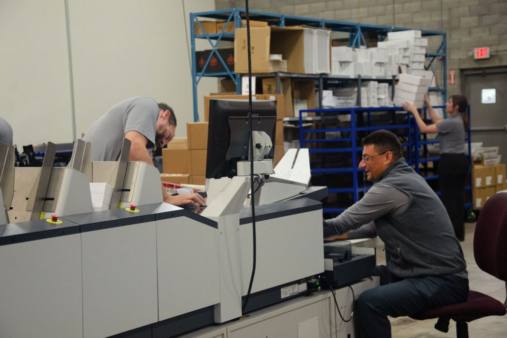 Mailstar team members running an inserting machine while a colleague stocks shelves