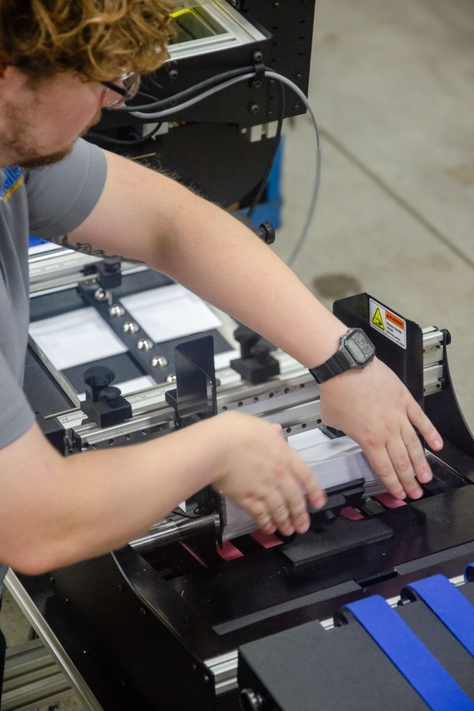 Production team member loading envelopes into an addressing machine feeder