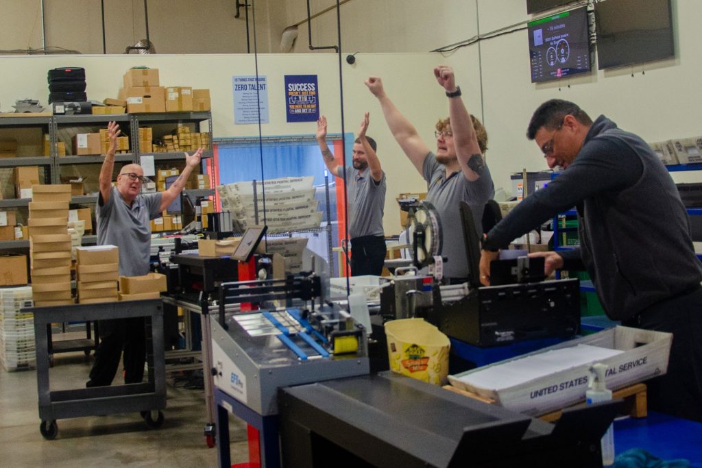 Mailstar production team celebrating with arms raised on the production floor