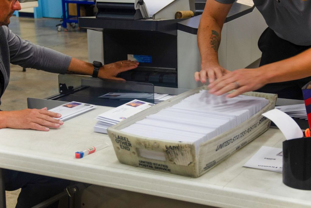 Hands feeding addressed envelopes from a USPS tray into a mailing machine